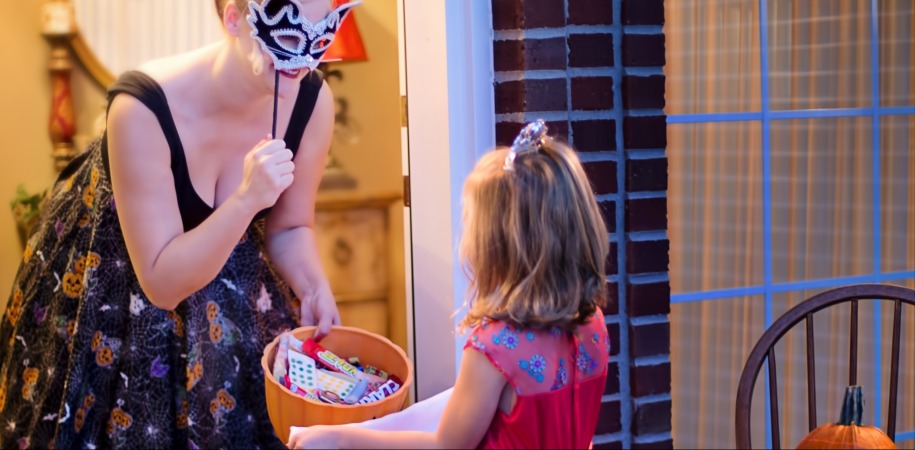 Young girl trick or treating and getting candy from a masked woman