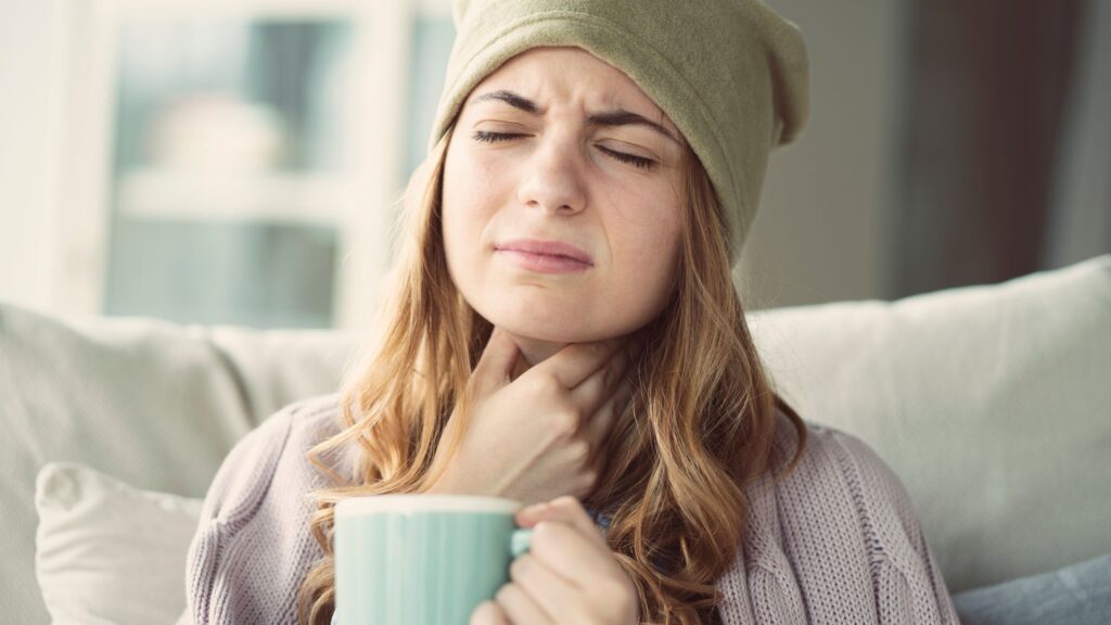 A women with a sore throat is drinking tea on the couch.